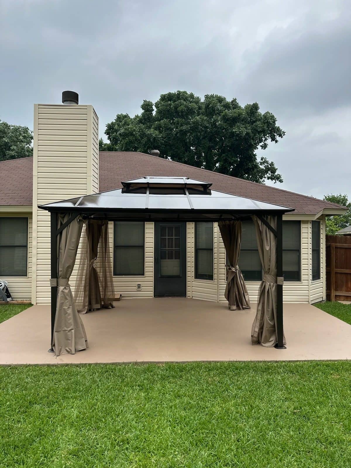 Double-roof metal gazebo with tan curtains tied back at each post on a backyard patio