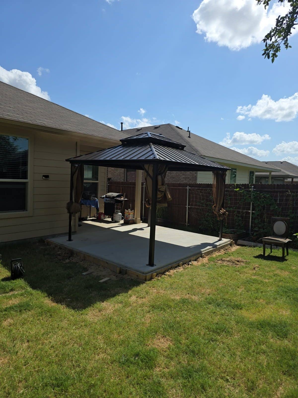 Metal hardtop gazebo assembled over a concrete patio behind a single-story house