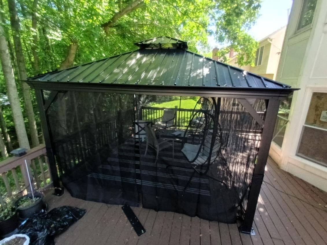 Hardtop gazebo with mosquito netting assembled on a raised wooden deck among trees