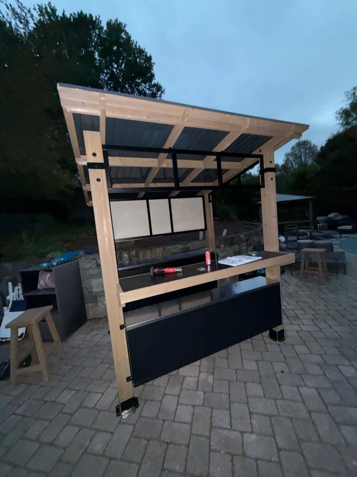 Wooden grill gazebo with a bar counter and shelves assembled on a paver patio