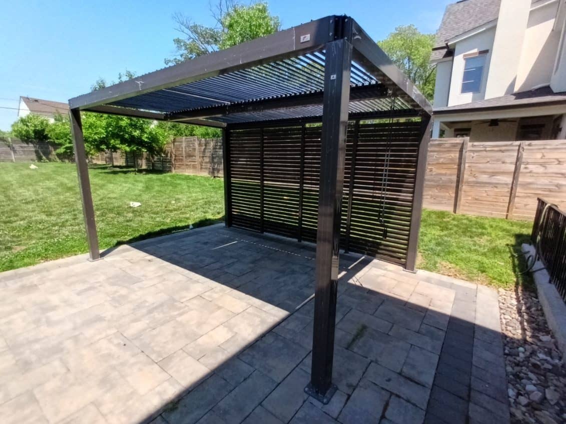 Dark aluminium louvered pergola with a slatted privacy wall on a paver patio