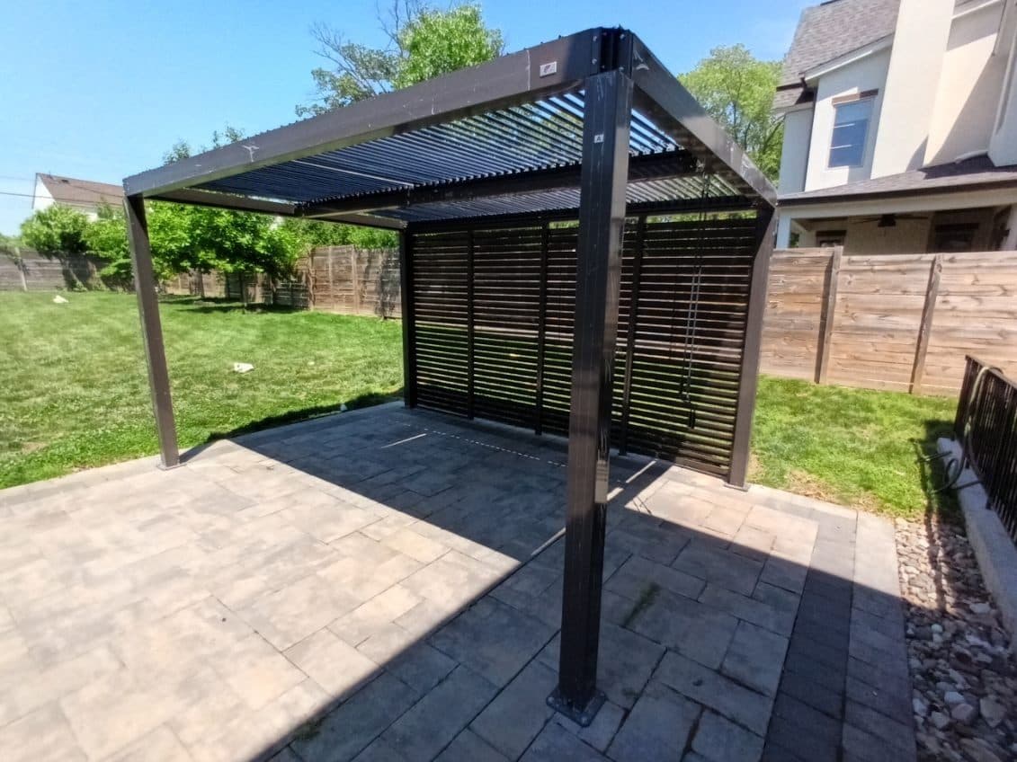 Dark aluminium louvered pergola with a slatted privacy wall on a paver patio