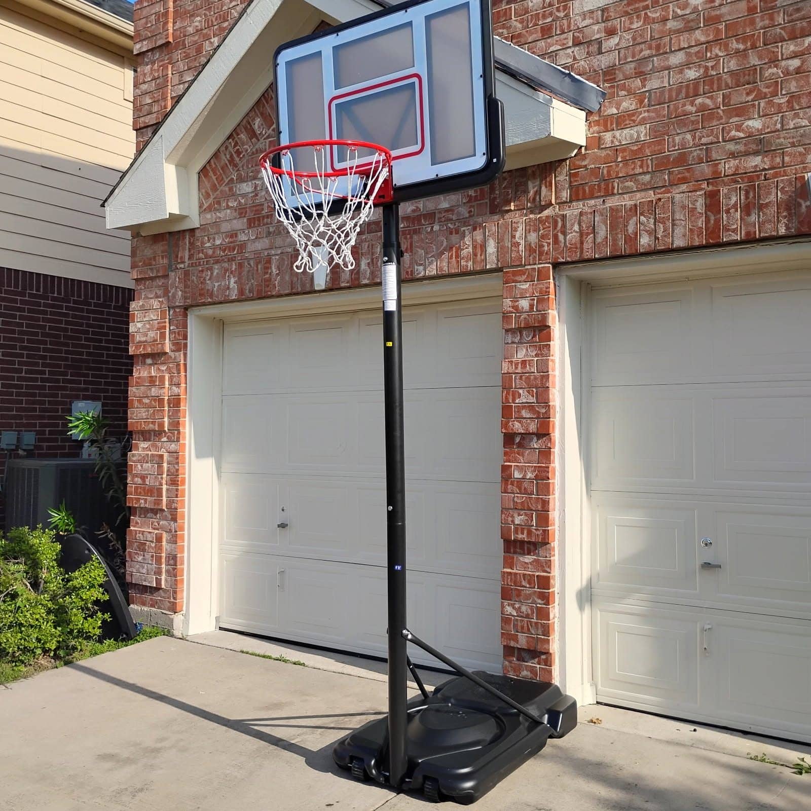 Portable basketball hoop with a filled base standing on a driveway in front of a garage
