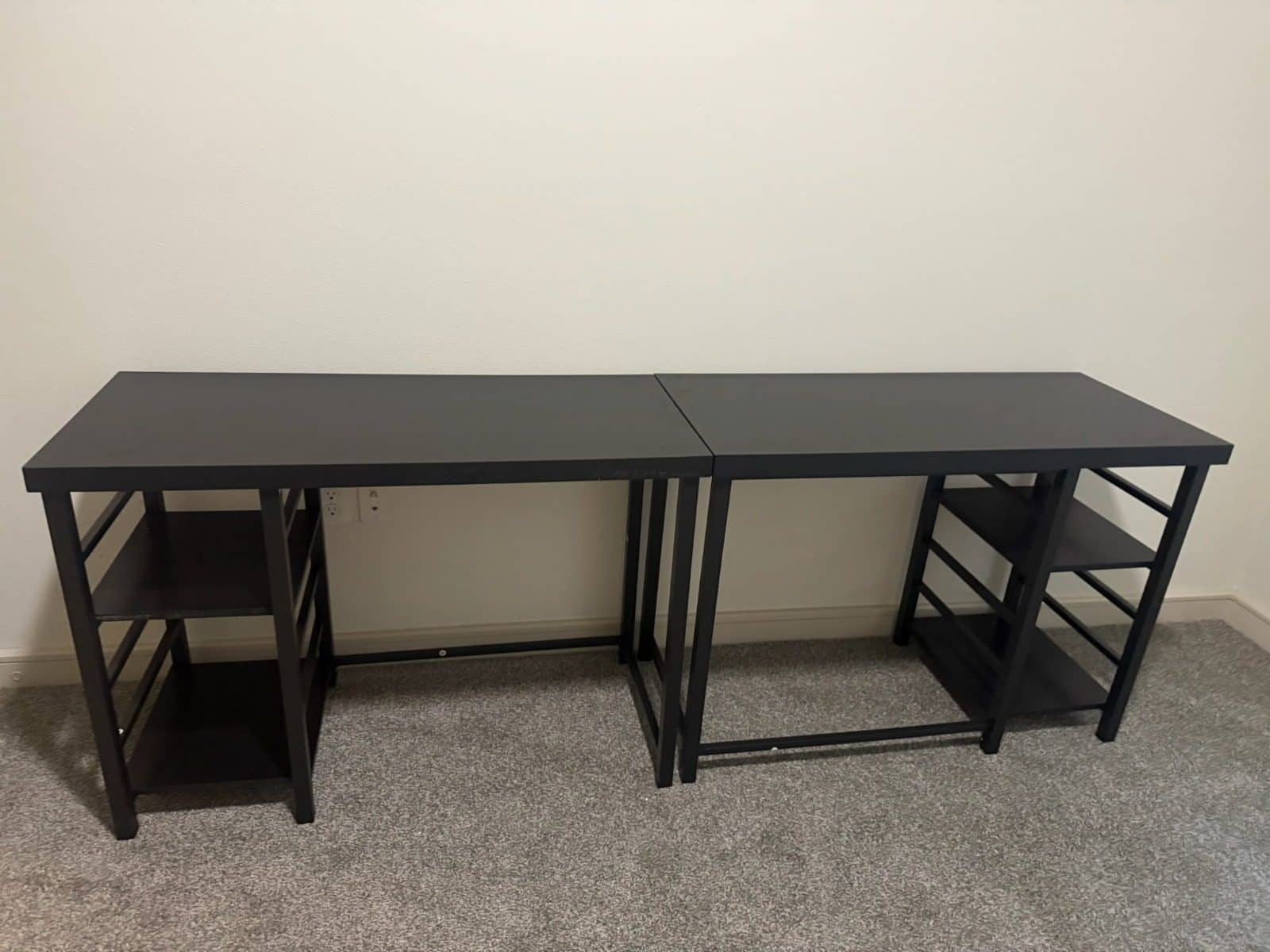 Two black desks with side shelves set end to end along a bedroom wall