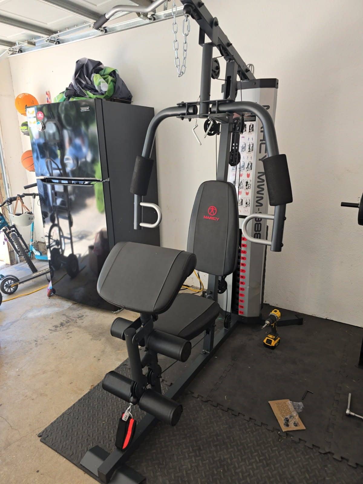 All-in-one home gym with a weight stack and padded seat assembled on garage floor mats