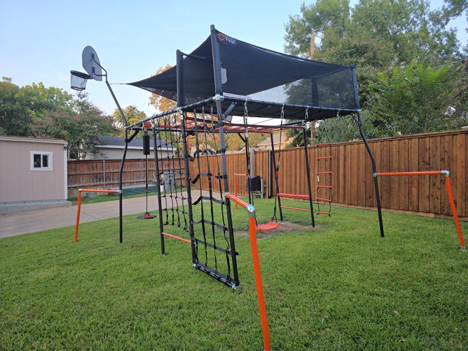 Metal climbing frame with a shade canopy, cargo net and swings on artificial turf